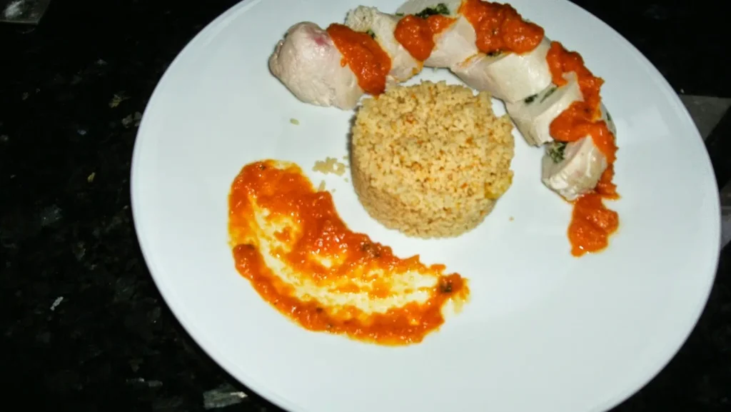 Poached chicken rounds with vibrant butternut squash sauce and couscous on a white plate at Casa Adora