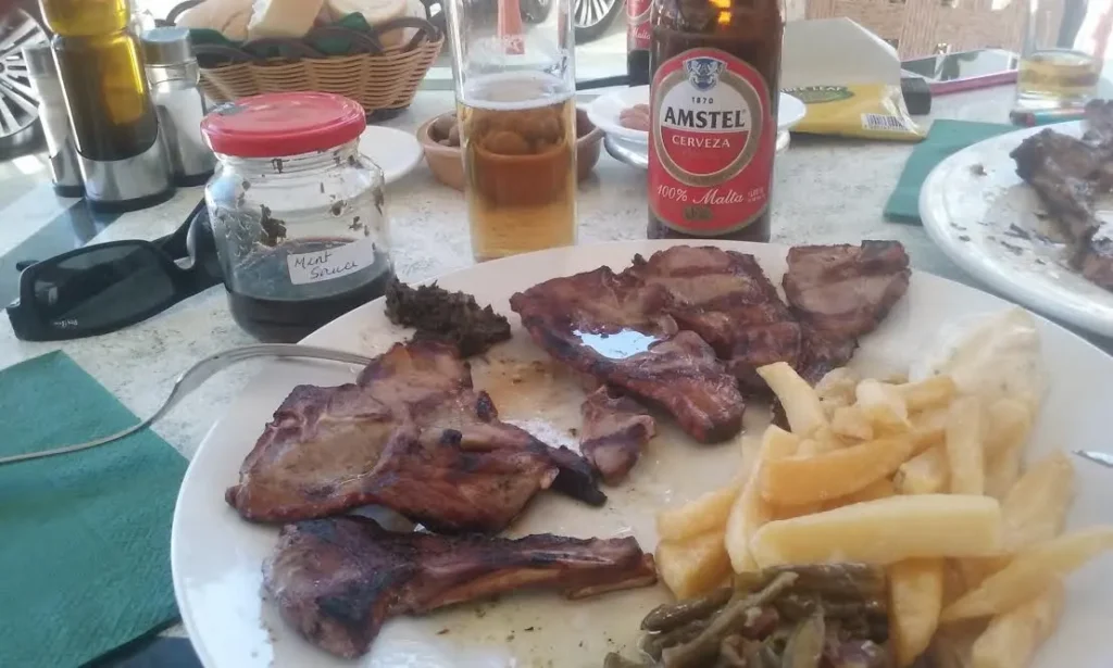 Grilled chuletillas de cordero with chips and green beans, homemade mint sauce jar on the table, Andalucía