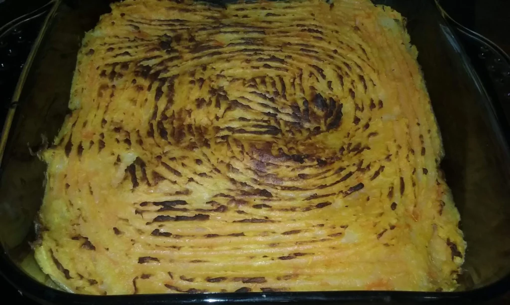 Sweet potato shepherd's pie fresh from the oven, golden forked topping with charred ridges in a glass baking dish