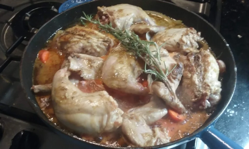 Two jointed wild rabbits braised with garlic, rosemary and white wine in a large pan on a gas hob – Casa Adora