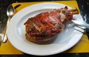 Baked shoulder of suckling pig on a white plate – paletilla de cochinillo – The Flexible Chef