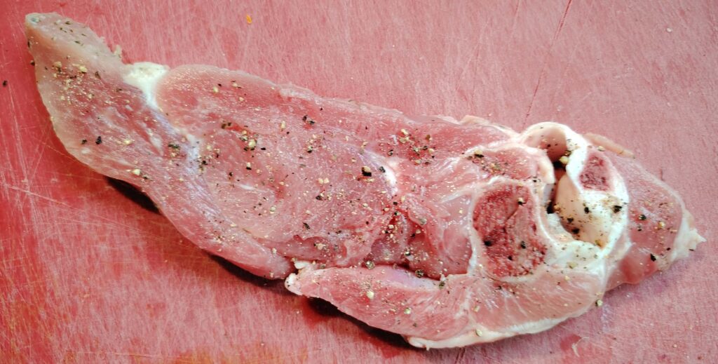 Garlic-marinated turkey chop seasoned with black pepper, resting on a red cutting board, ready for searing.