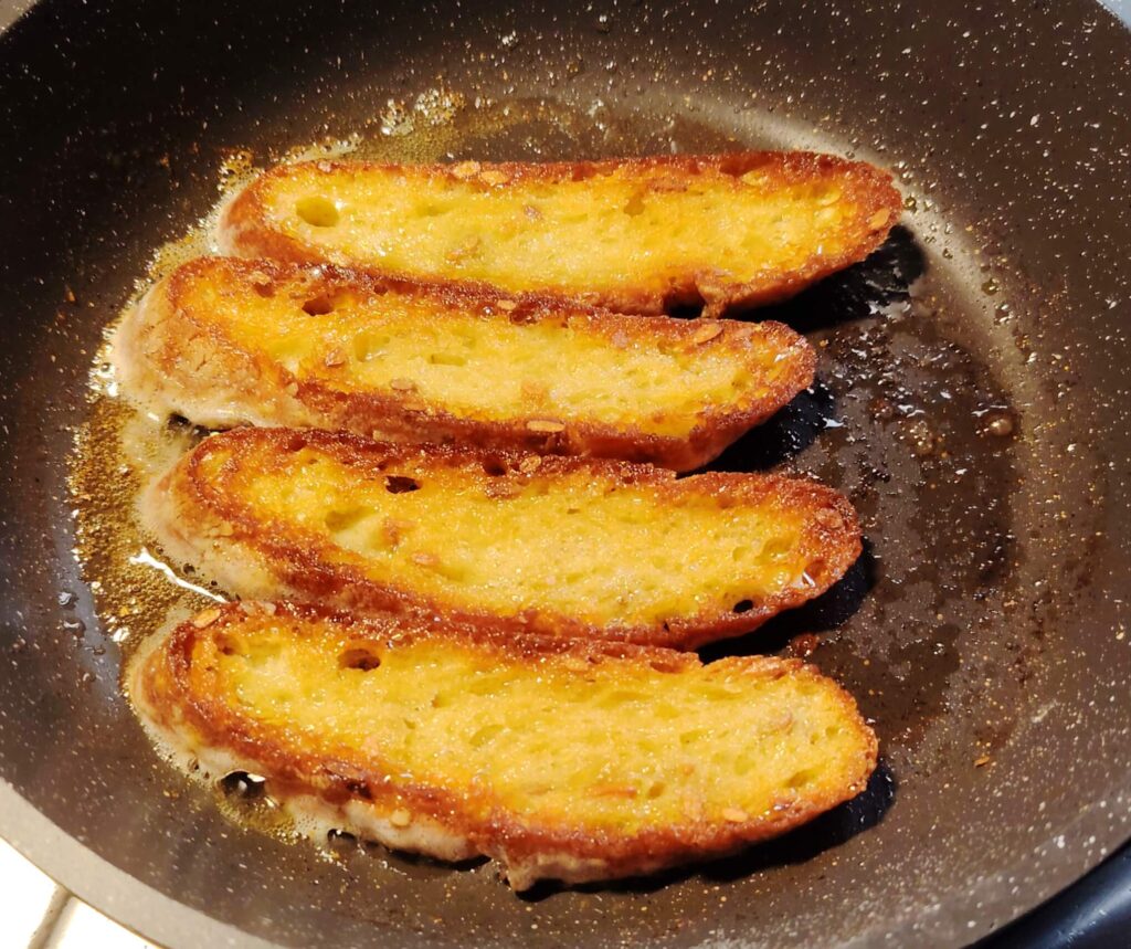 Four pieces of sourdough gently frying in a pan with olive oil and butter.