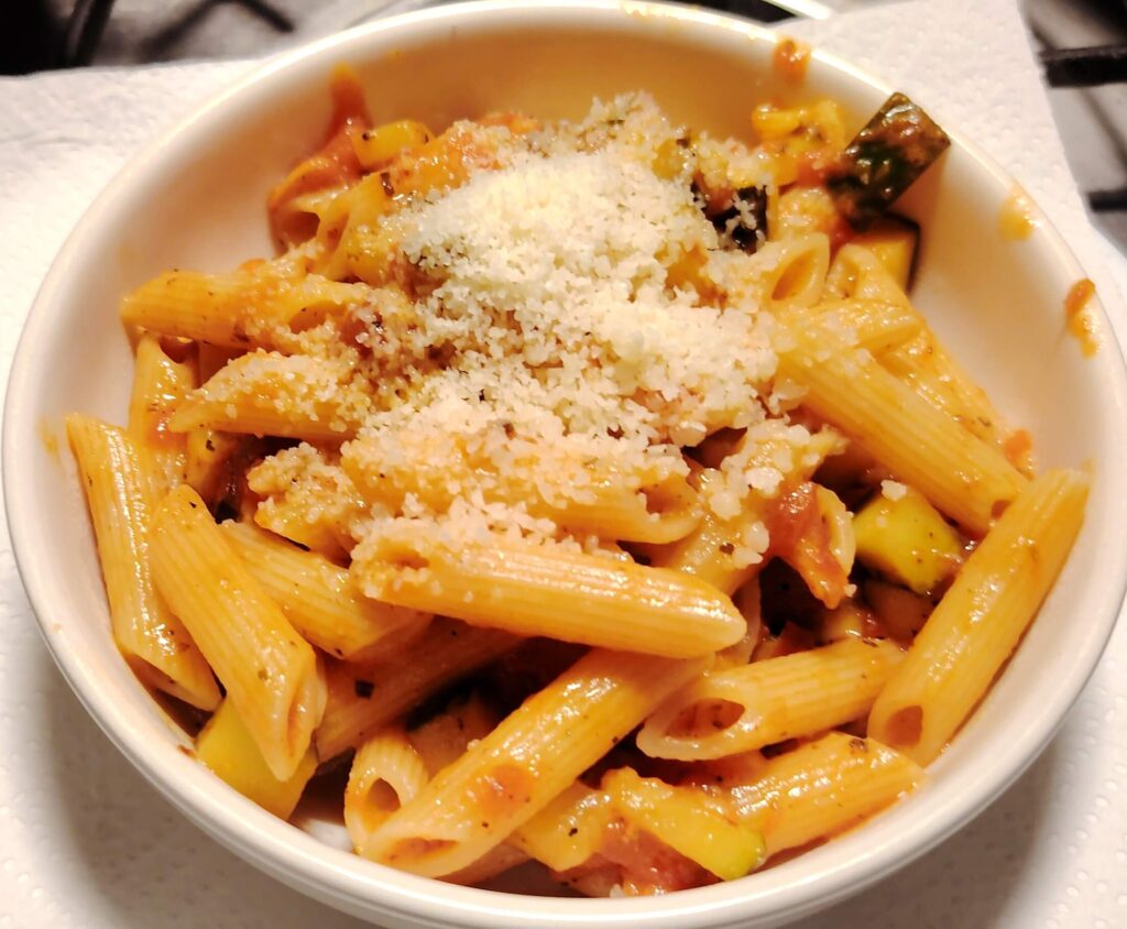 A white bowl of pasta in tomato sauce topped with parmesan cheese