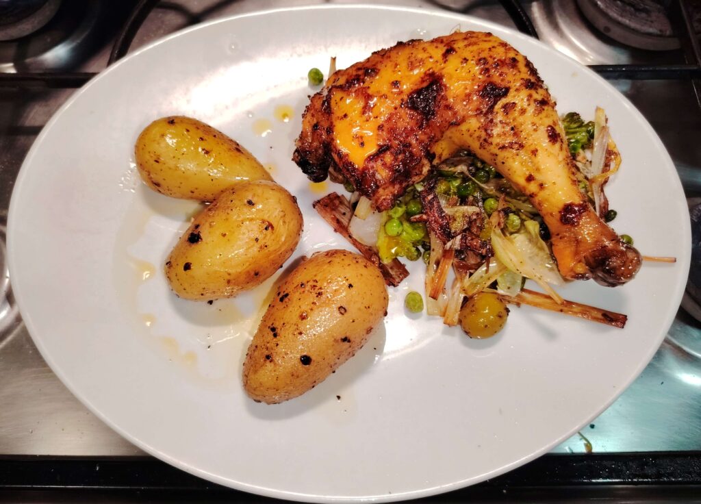 Roasted chicken leg quarter served with golden new potatoes and sautéed leeks and peas. A hearty, home-cooked meal with crispy skin and rustic charm.