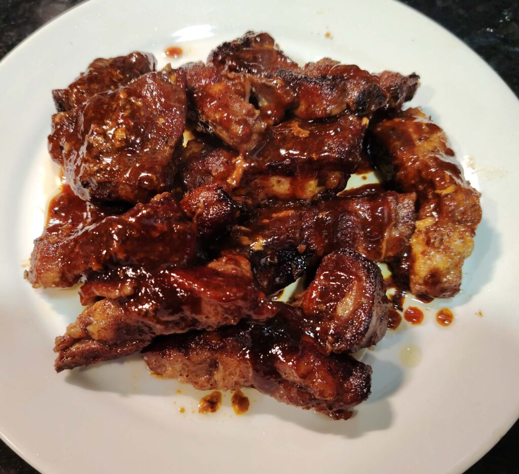 Cooked Char Siu Pork Ribs on a white plate smothered in hoisin sauce.