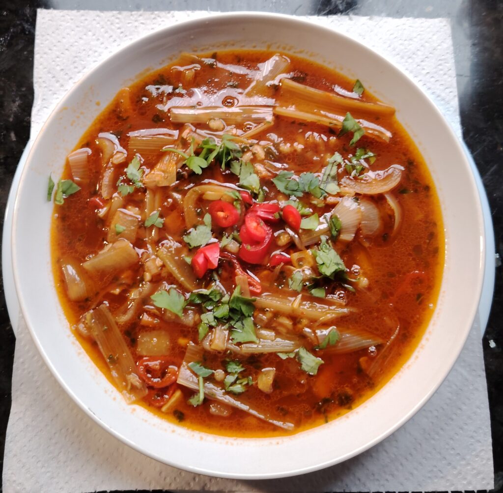 A white soup bowl with prawn, Chilli, tomato broth.