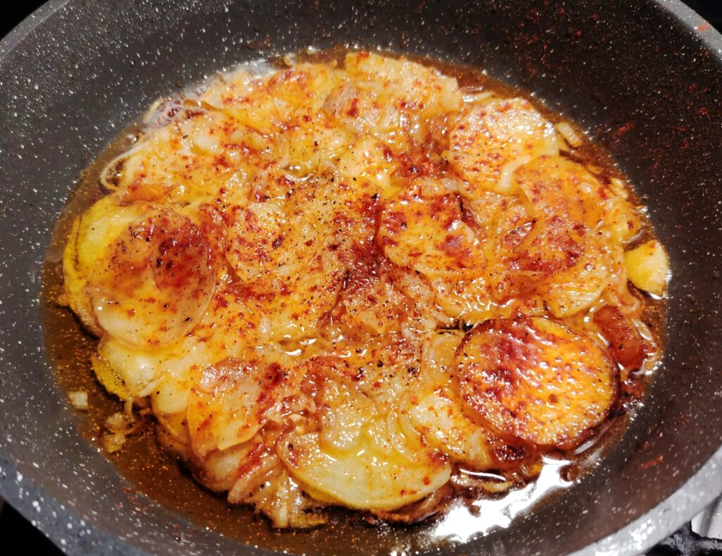 Sliced potatoes and onions gently poaching in olive oil