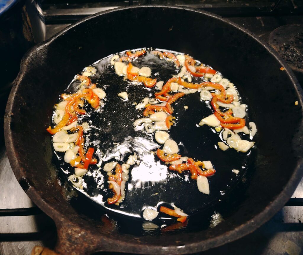 Sliced red peppers and garlic sautéing in olive oil in cast iron skillet