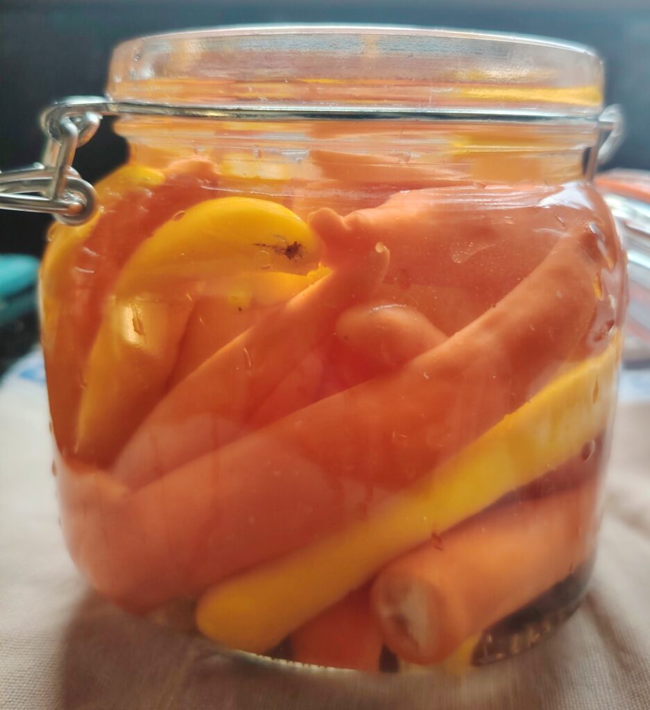 A clasp‑lid glass jar filled with orange and yellow chillies submerged in brine, sitting on a light cloth in the Casa Adora kitchen.