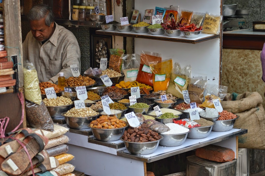 A spice and dry goods trader at his stall in Chandni Chowk market, Delhi, with bowls of nuts, dried fruits and spices on display.