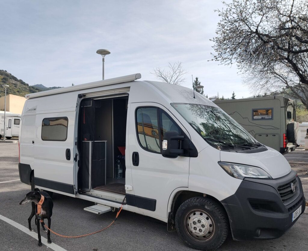 Campervan parked at the área de autocaravanas in Cabra, Córdoba, Andalucía, with a black Galgo Español on a lead alongside.