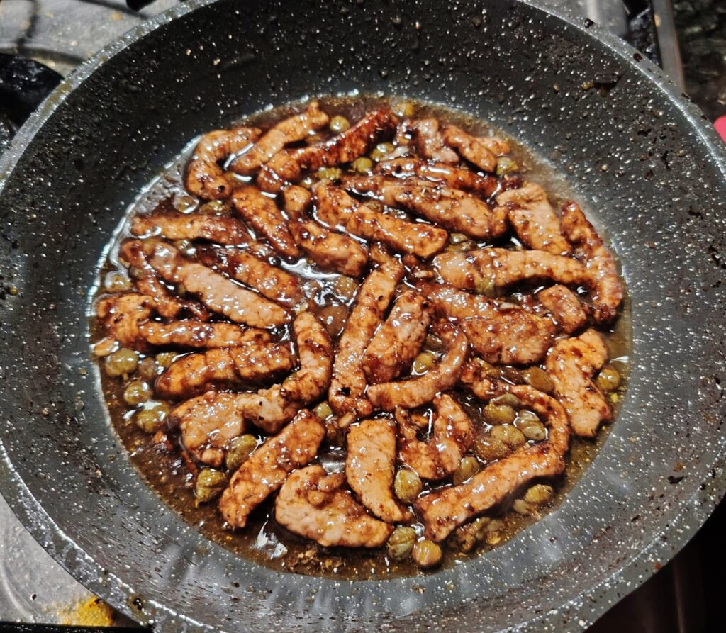 Pan fried veal in balsamic with capers — sizzling in a frying pan with a rich dark glaze