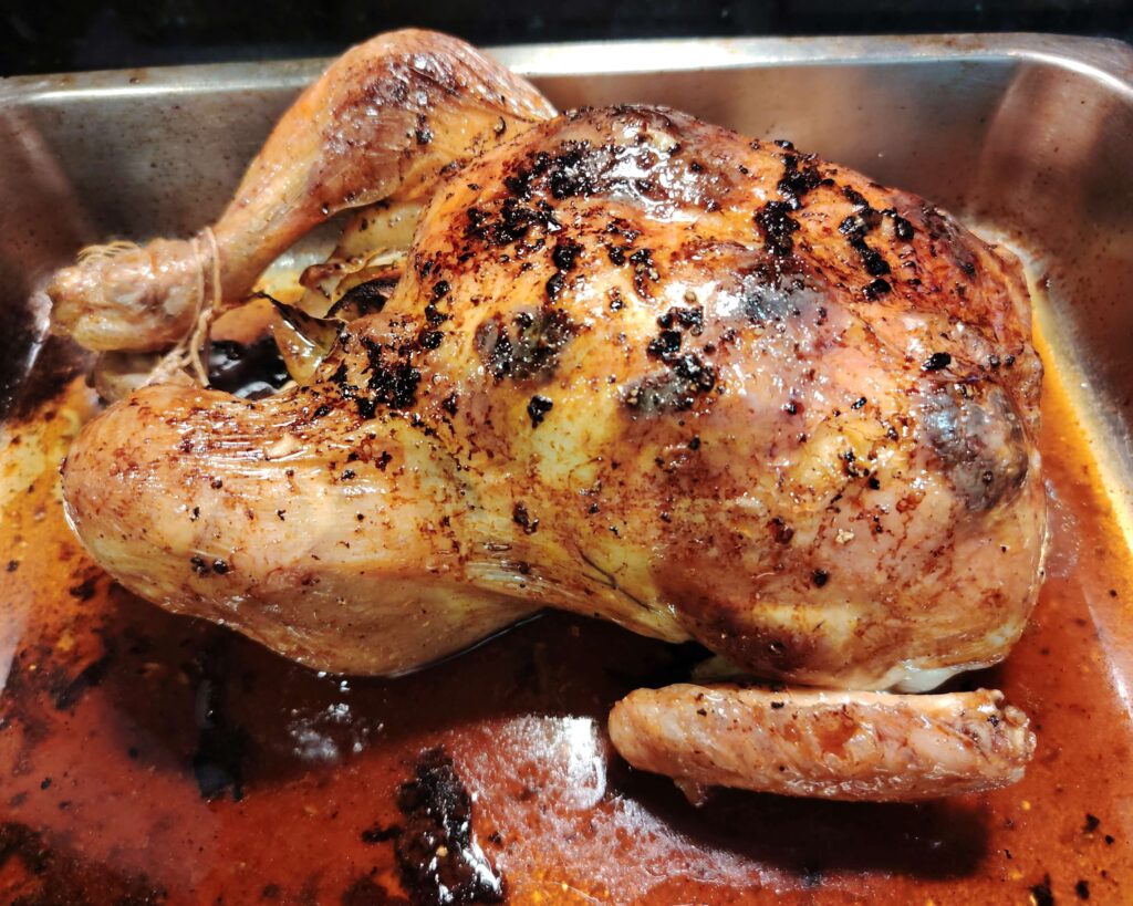 Golden roast chicken for one with confit garlic butter, resting in roasting tin with pan juices