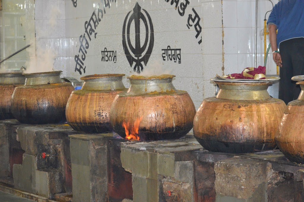 Large copper cooking pots bubbling over open flames in a Sikh Gurdwara langar kitchen in India — free food prepared daily for anyone in need.