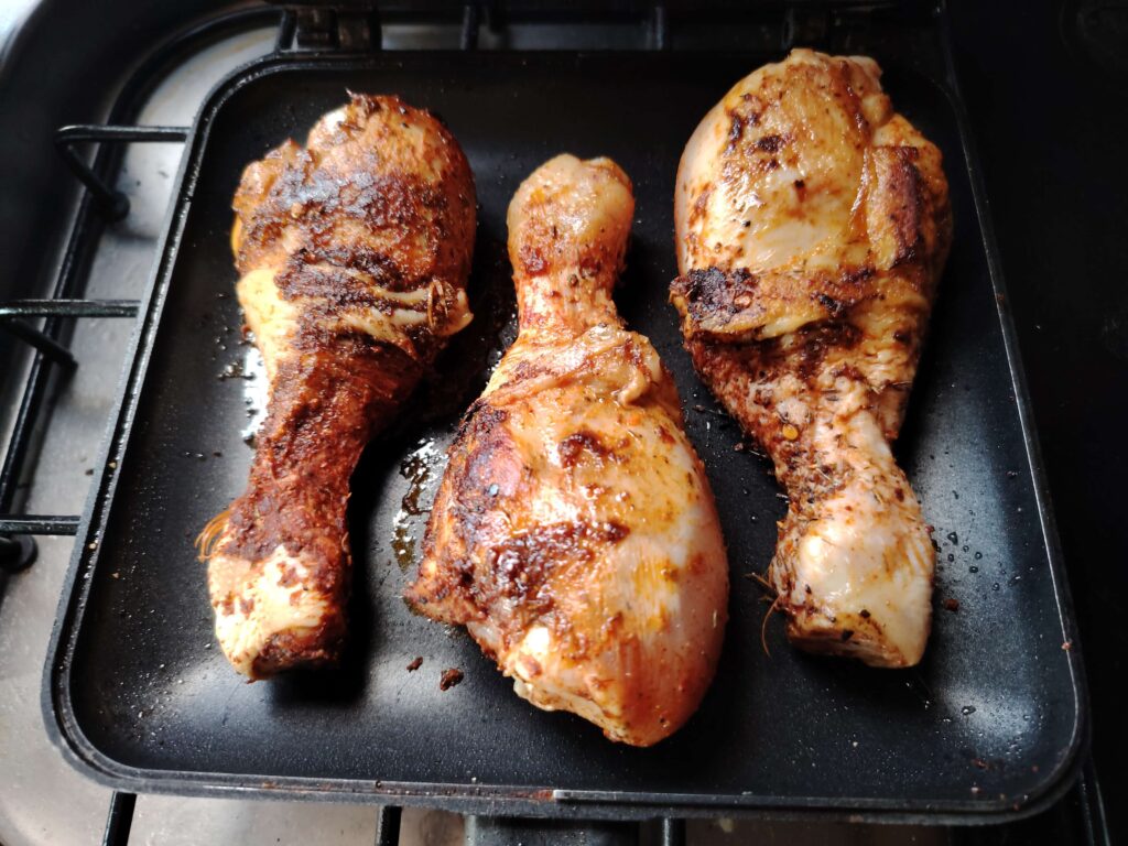 Three spiced chicken drumsticks browning in a RidgeMonkey pan on a campervan gas hob