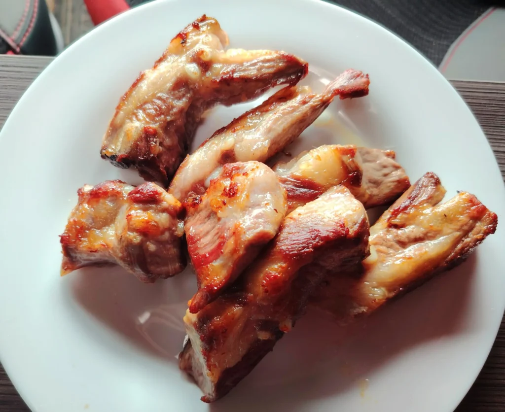 Beer-braised Ibérico pork ribs on a white plate, glazed and caramelised, cooked in one pan at Hermoso Campo in Extremadura.