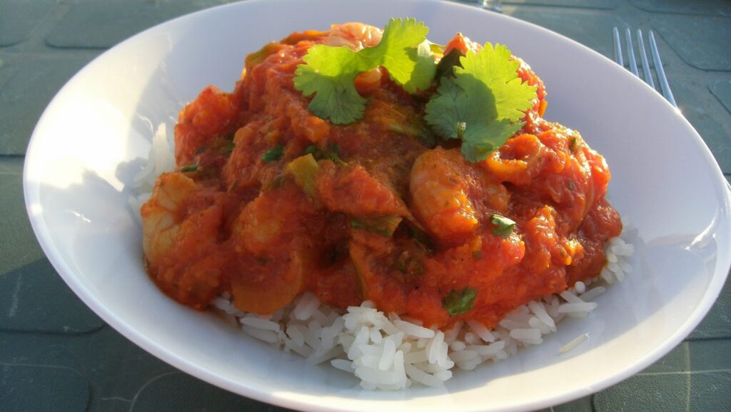 A vibrant Red Thai Prawn Curry with fresh mango slices, green beans, and red chillies served in a shallow white bowl.