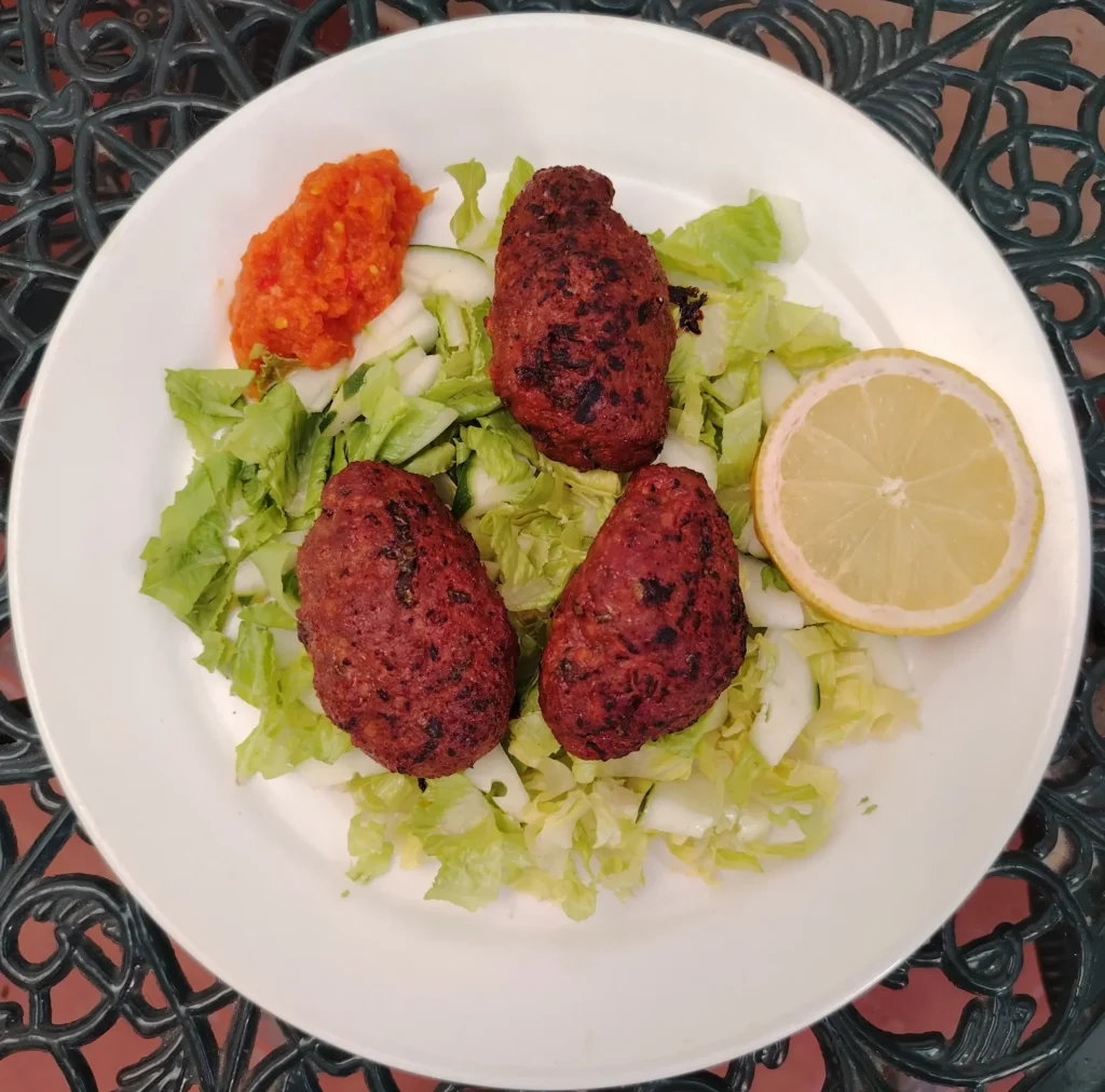 Three grilled Andalucían beef kebabs on shredded lettuce with hot sauce and a lemon wedge