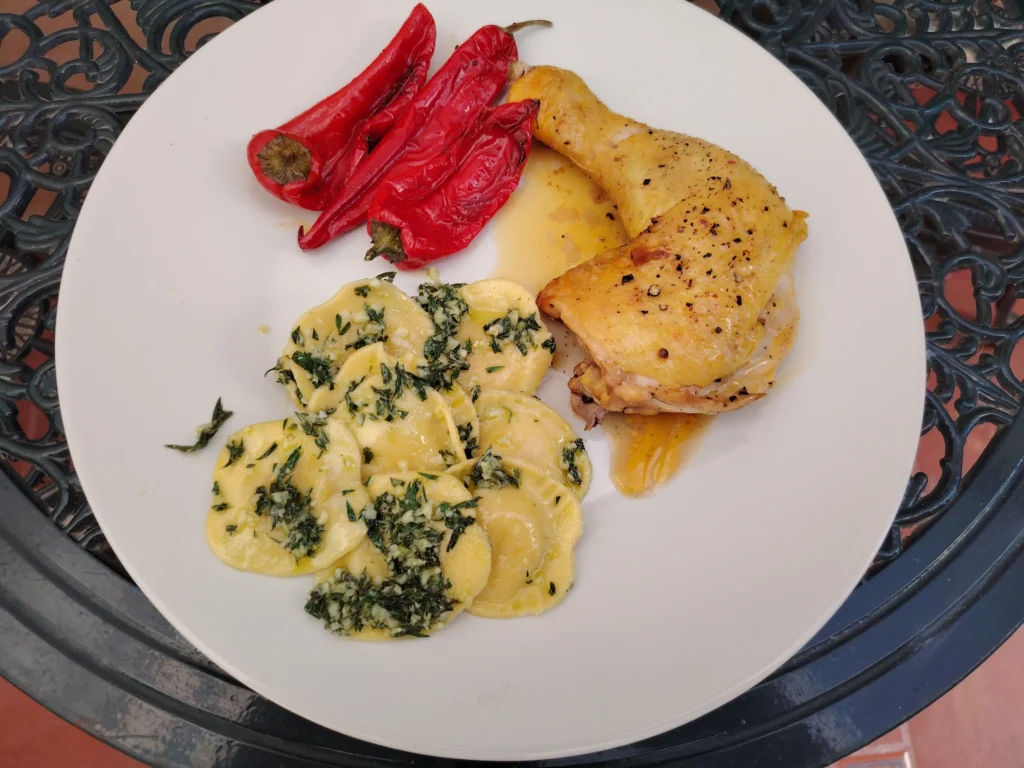 Cold pan chicken leg with carrot top pesto ravioli and blistered red peppers on a white plate