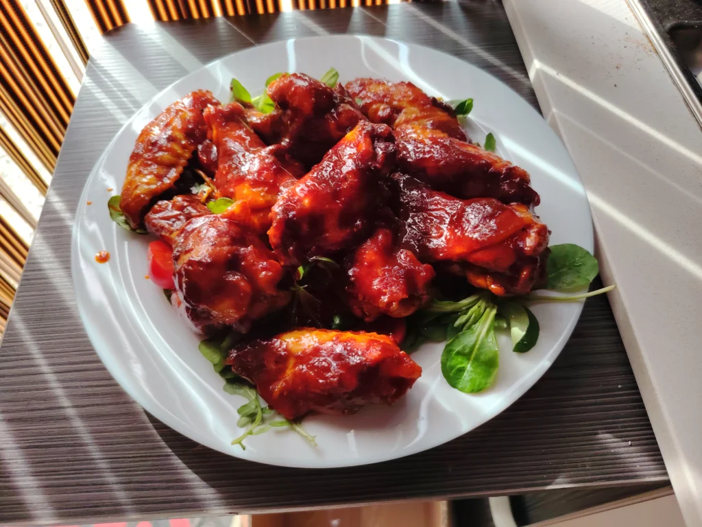 Sticky glazed chicken wings served on a white plate with lamb's lettuce — van kitchen, Noalejo