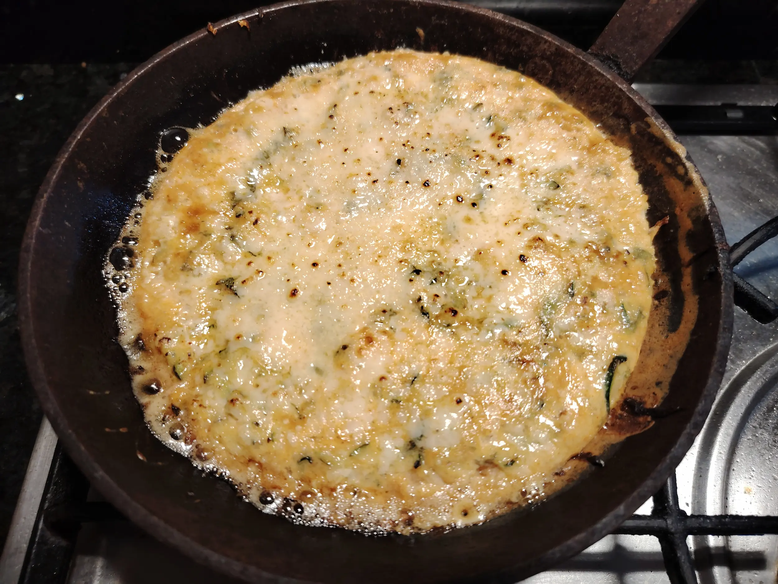 Courgette and cheddar frittata browned under a flame gun in a cast-iron skillet