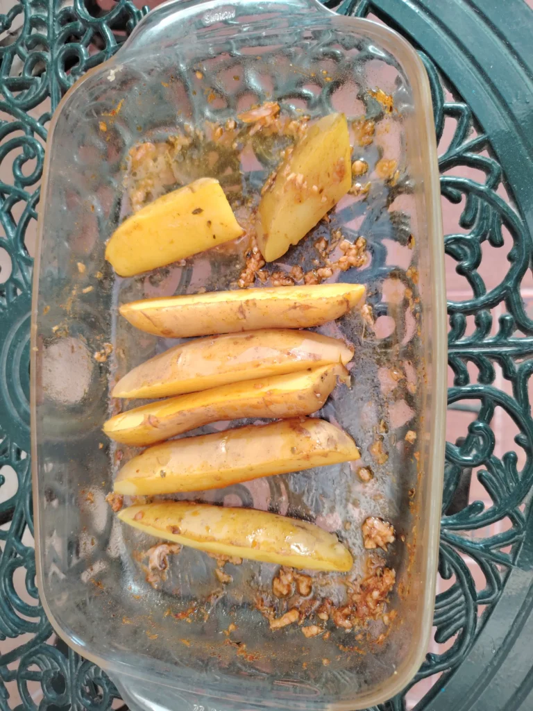 Par-boiled Cyprus potato wedges tossed in leftover chicken souvlaki marinade in a glass dish