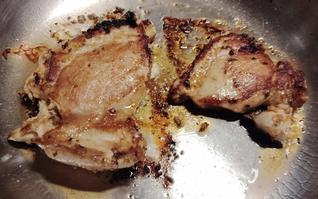 Marinated chicken souvlaki thighs cooking in a stainless steel frying pan
Caption: No plancha needed — a hot stainless steel pan gives you the same result