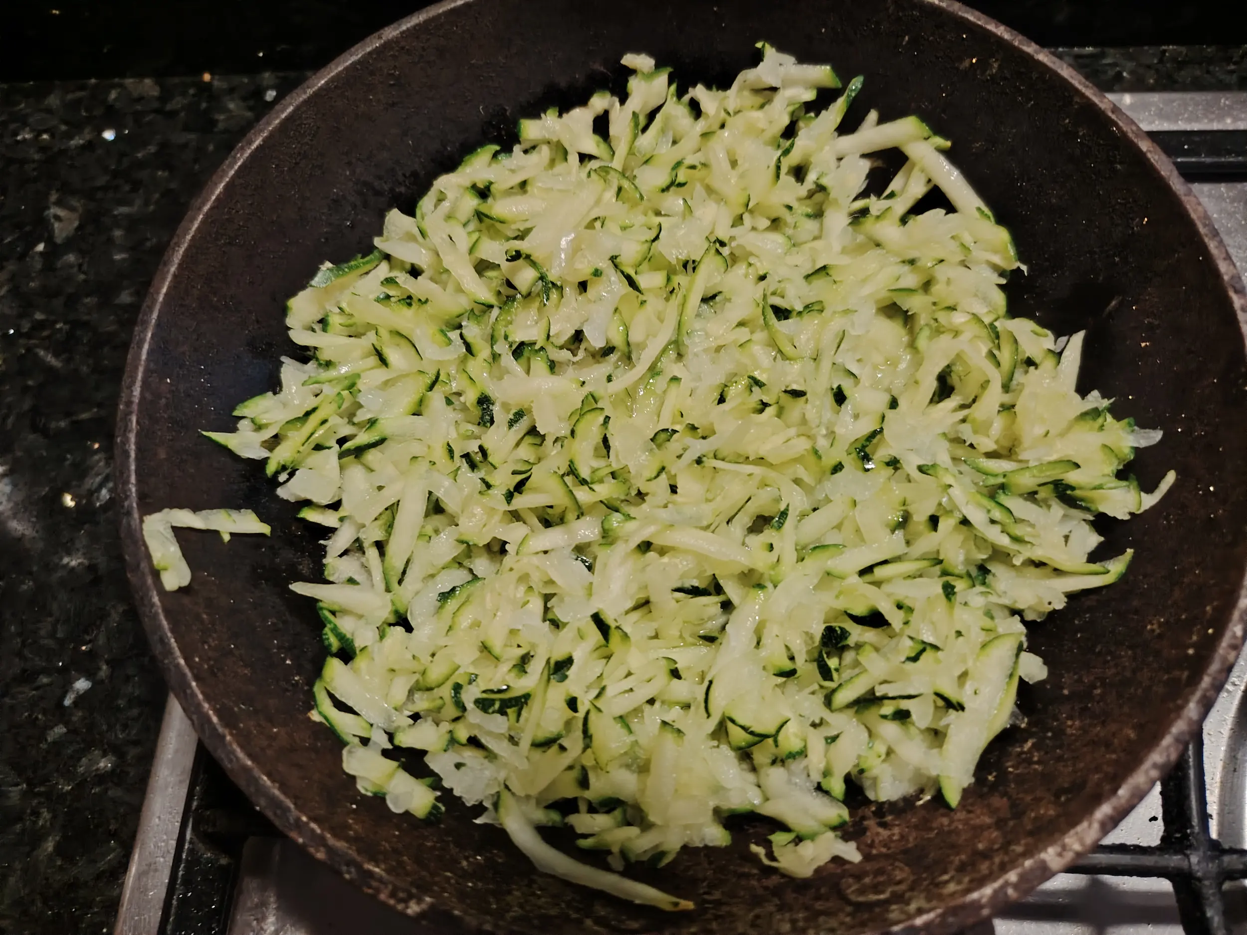 Grated courgette and onion in a cast-iron skillet before cooking for a frittata