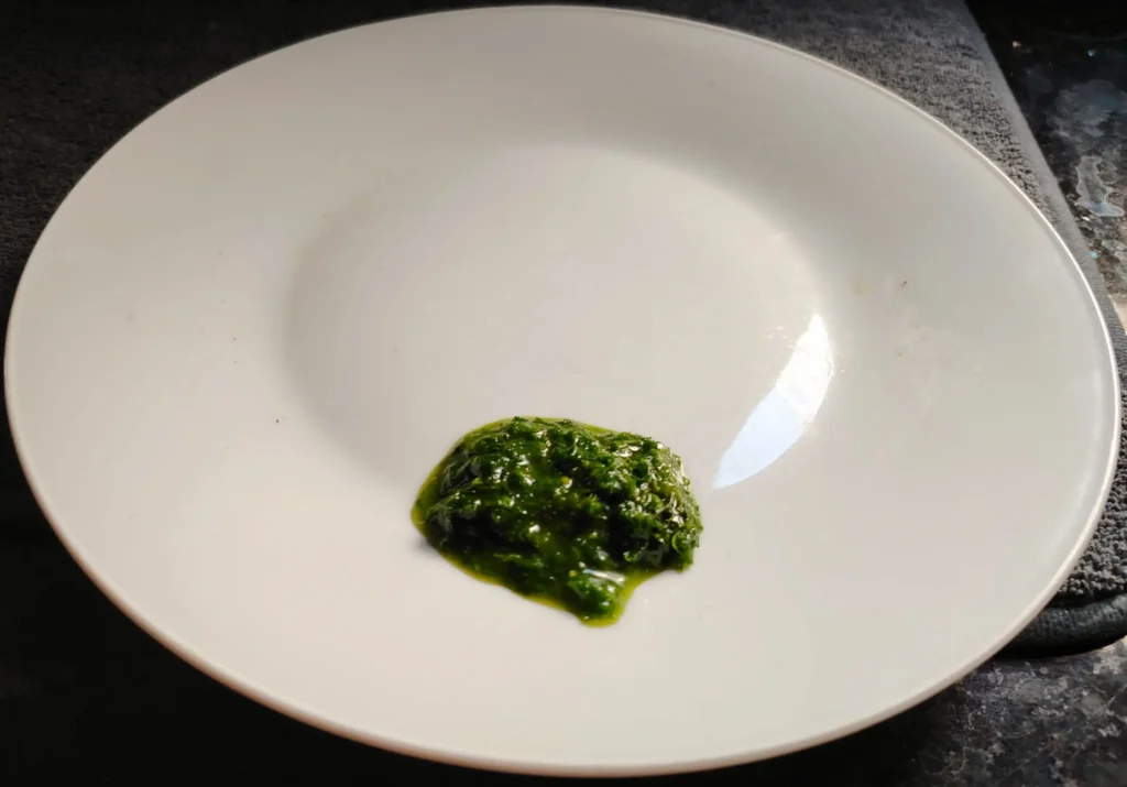 Kale dressing spooned onto a white plate on a black speckled granite worktop — vivid green, glossy, slightly rough in texture