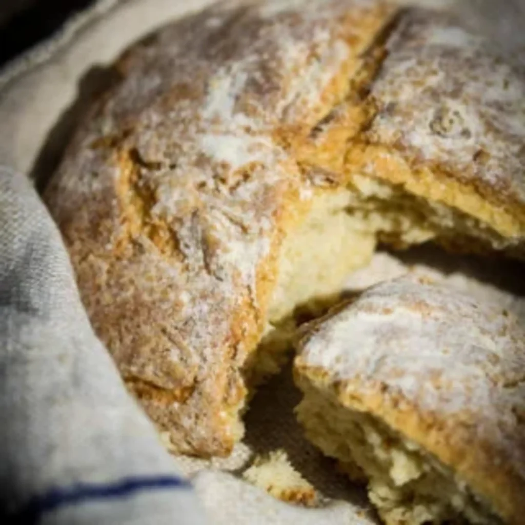Fife bannock Scottish soda bread broken open into quarters and partially wrapped in a linen tea towel on a black speckled granite worktop — flour-dusted golden crust
