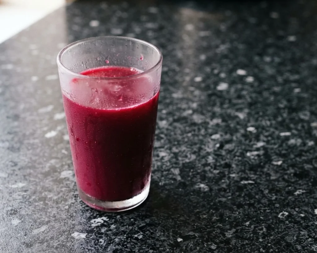 Beetroot juice recipe — deep crimson-purple beetroot, carrot and ginger juice in a condensation-cold glass on a black speckled granite worktop at Casa Adora