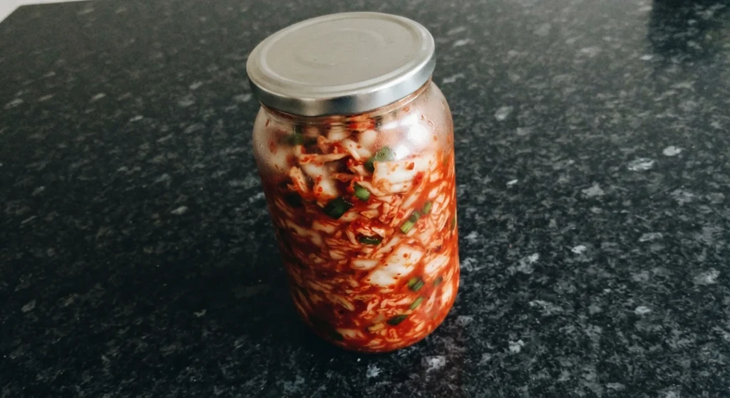 Homemade kimchi recipe in a 750ml jar — white cabbage with pimentón and spring onions on black speckled granite
