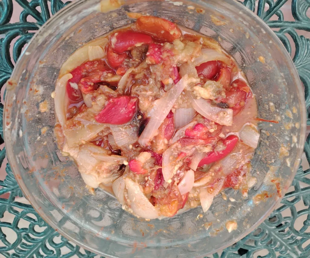 Fire-roasted red peppers, tomatoes, onion, and aubergine combined in a glass bowl — ready to blend into homemade lutenitsa