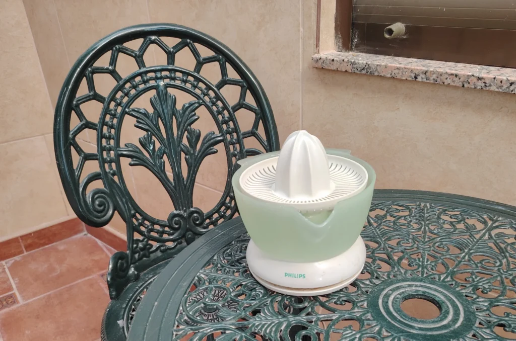 Philips citrus juicer on the Andaluz patio table at Casa Adora — green cast iron furniture, terracotta tiles