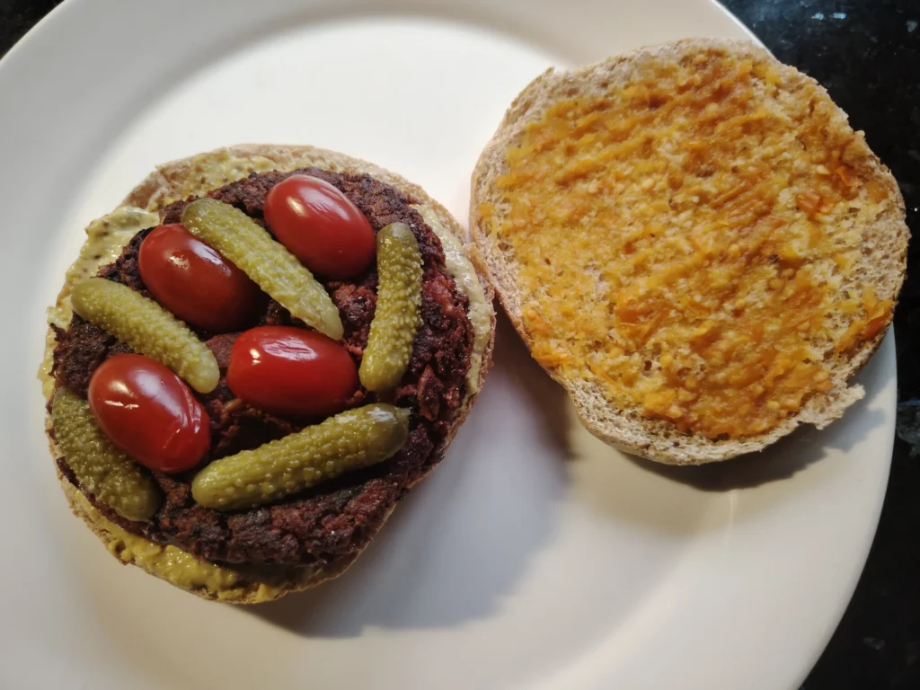 Beetroot burger recipe — black bean and beetroot burger in a wholemeal bun with remoulade, Tropical Sunset hot sauce, cornichons and cherry tomatoes, black speckled granite worktop
