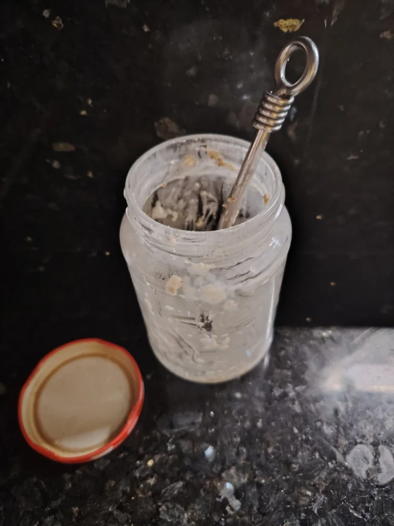 Empty glass jar with red lid after overnight buckwheat breakfast — Casa Adora kitchen, black granite worktop