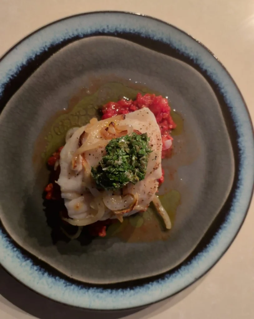 Danny's roasted cod with chorizo and potatoes, finished with parsley and garlic salsa, served in a blue-grey bowl