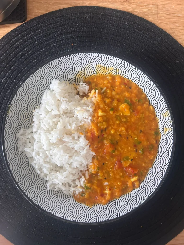 Lentil dhal recipe — red lentil dhal with white rice in a patterned bowl on a black woven placemat, Rochdale