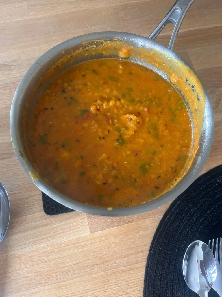 Red lentil dhal in a stainless steel saucepan on a wooden worktop, Rochdale