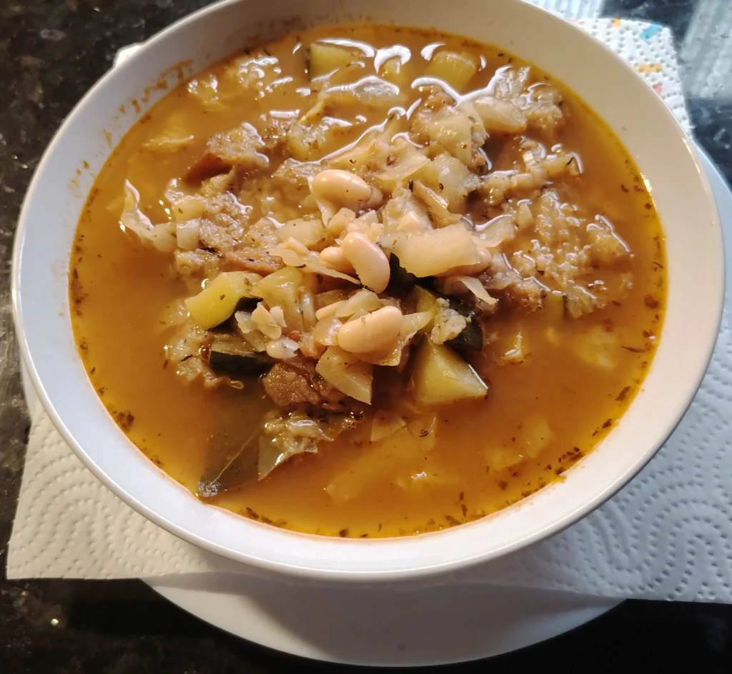 Ribollita recipe — Tuscan white bean and cabbage soup thickened with stale buckwheat sourdough in a white bowl on a black granite worktop