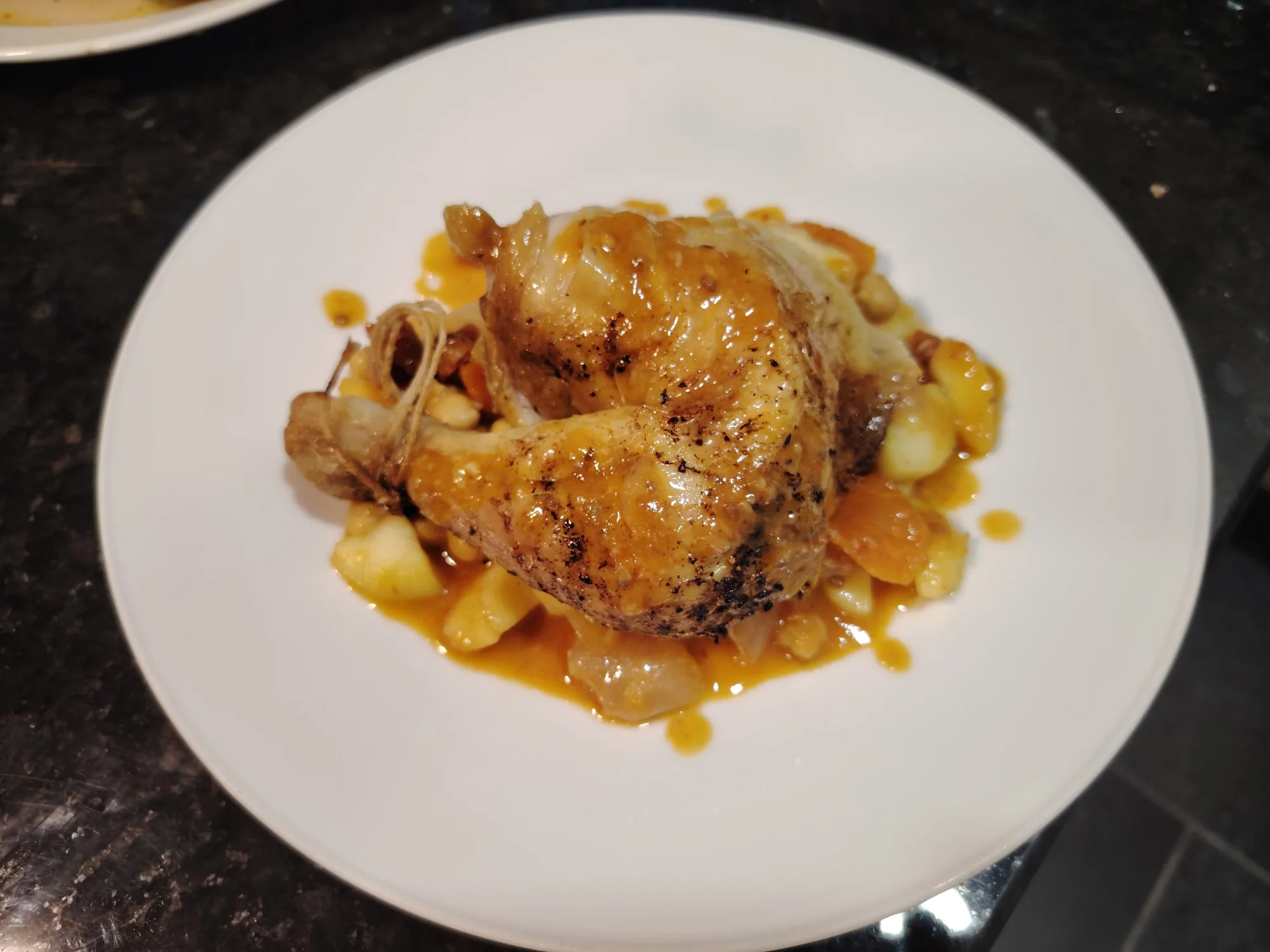 Crisp-skinned roast chicken leg served on a white bean, chickpea and pepino stew on a white plate