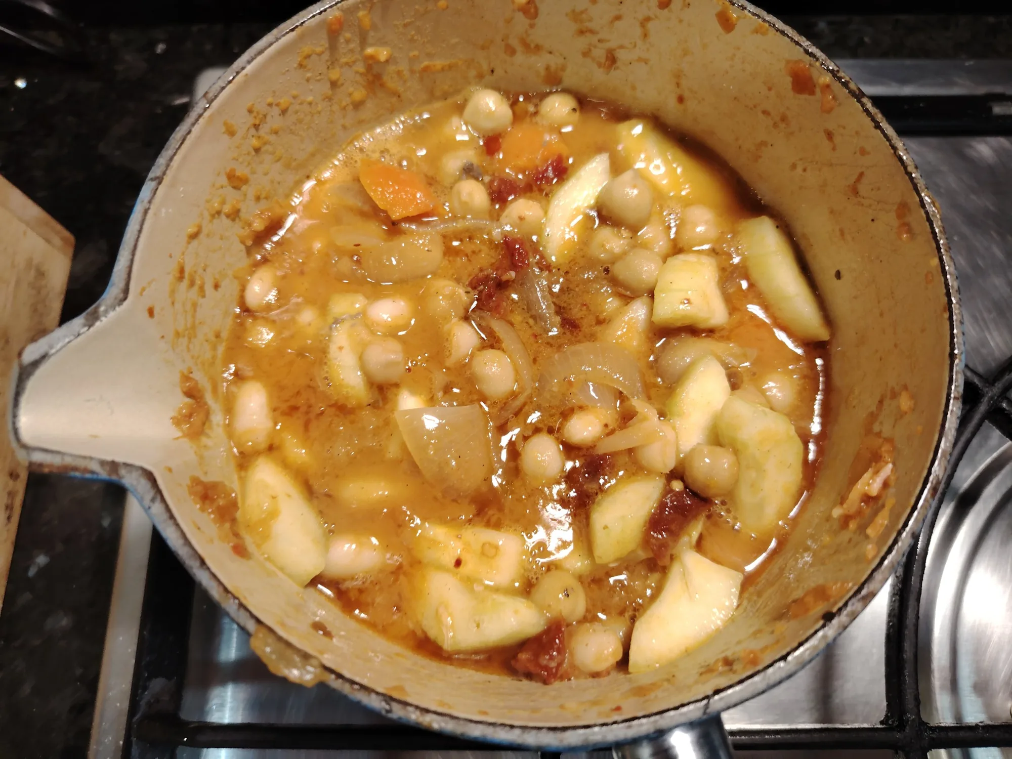 White beans, chickpeas, pepino, sun-dried tomato, carrot and onion in a golden pan-juice sauce in a cream enamel saucepan